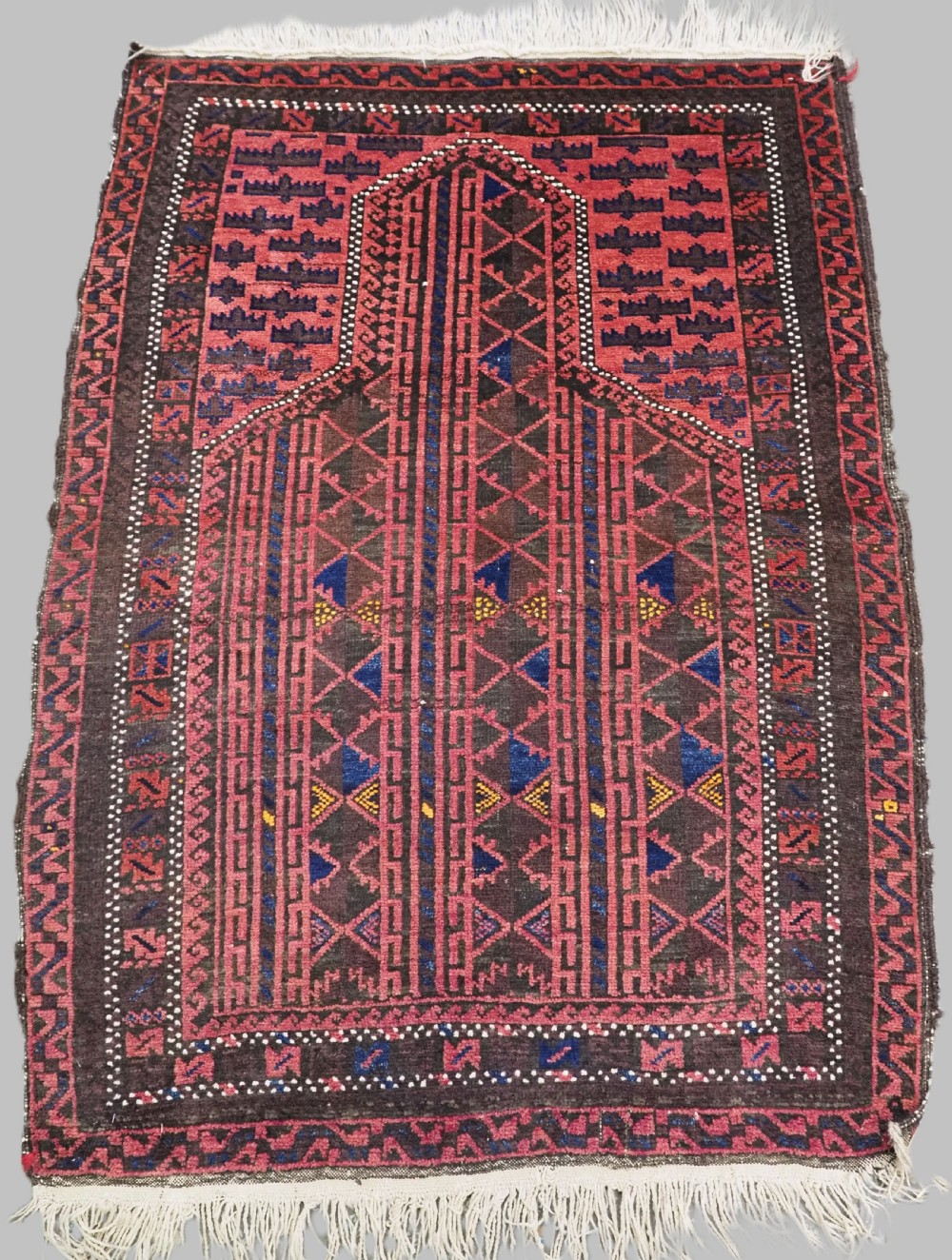 An antique Afghan wool prayer rug displaying a dark brown field with geometric lattice patterns framed by a terracotta arch motif.