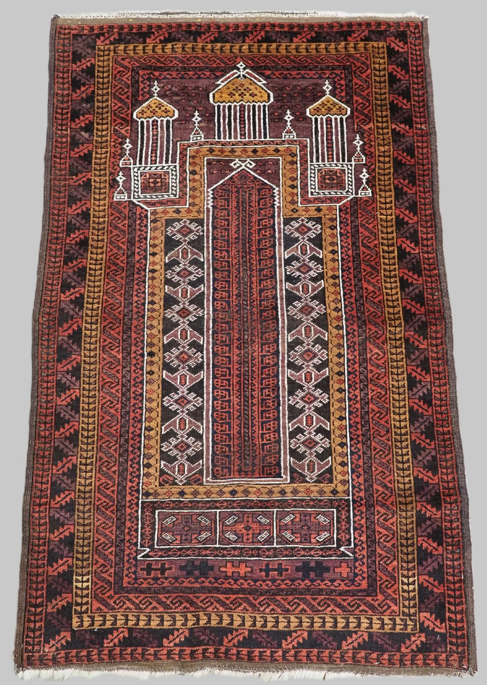 An antique hand-knotted Afghan Baluch wool prayer rug featuring a triple mihrab architectural design in burgundy, brown, ochre, and white tones.