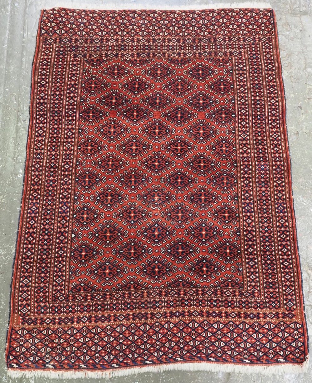 A hand-knotted wool Yomut Turkmen rug featuring a deep red field decorated with a dense repeating lattice pattern in navy, ivory, and brown tones.