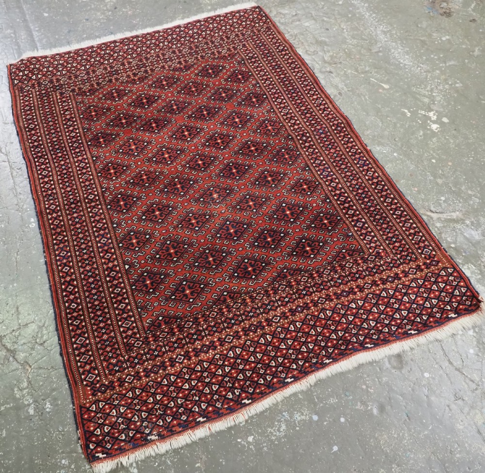 A hand-knotted wool Yomut Turkmen rug featuring a deep red field decorated with a dense repeating lattice pattern in navy, ivory, and brown tones. View II