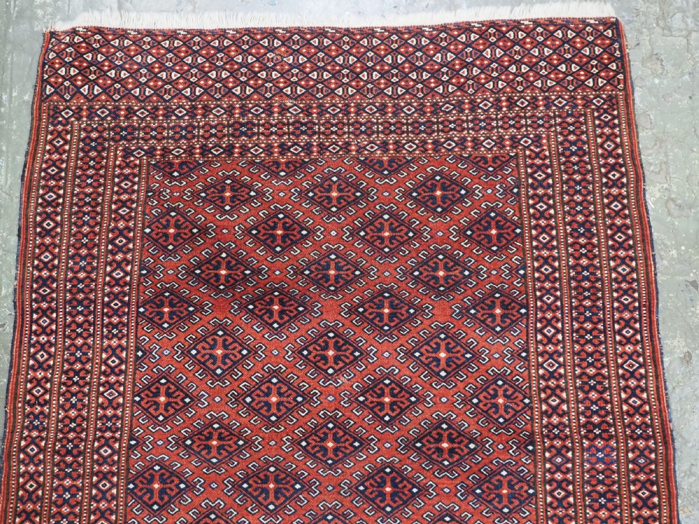 A hand-knotted wool Yomut Turkmen rug featuring a deep red field decorated with a dense repeating lattice pattern in navy, ivory, and brown tones. View III