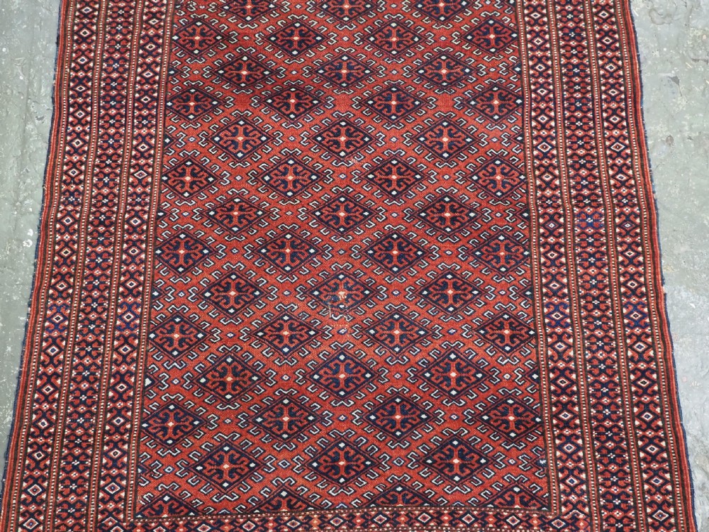 A hand-knotted wool Yomut Turkmen rug featuring a deep red field decorated with a dense repeating lattice pattern in navy, ivory, and brown tones. View IV