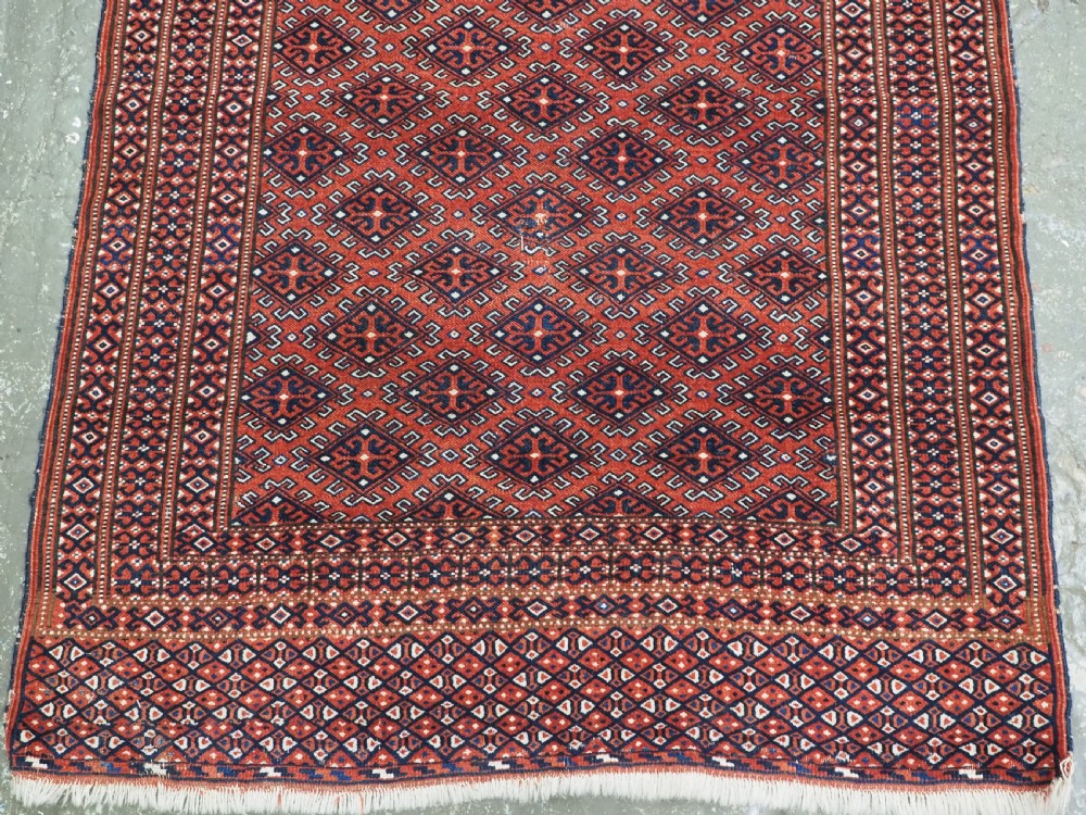 A hand-knotted wool Yomut Turkmen rug featuring a deep red field decorated with a dense repeating lattice pattern in navy, ivory, and brown tones. View VI
