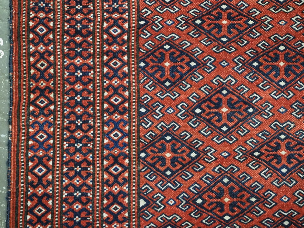A hand-knotted wool Yomut Turkmen rug featuring a deep red field decorated with a dense repeating lattice pattern in navy, ivory, and brown tones. View VII