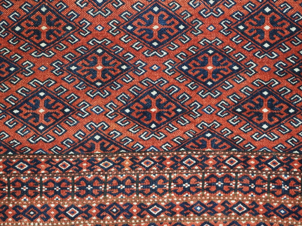 A hand-knotted wool Yomut Turkmen rug featuring a deep red field decorated with a dense repeating lattice pattern in navy, ivory, and brown tones. View IX