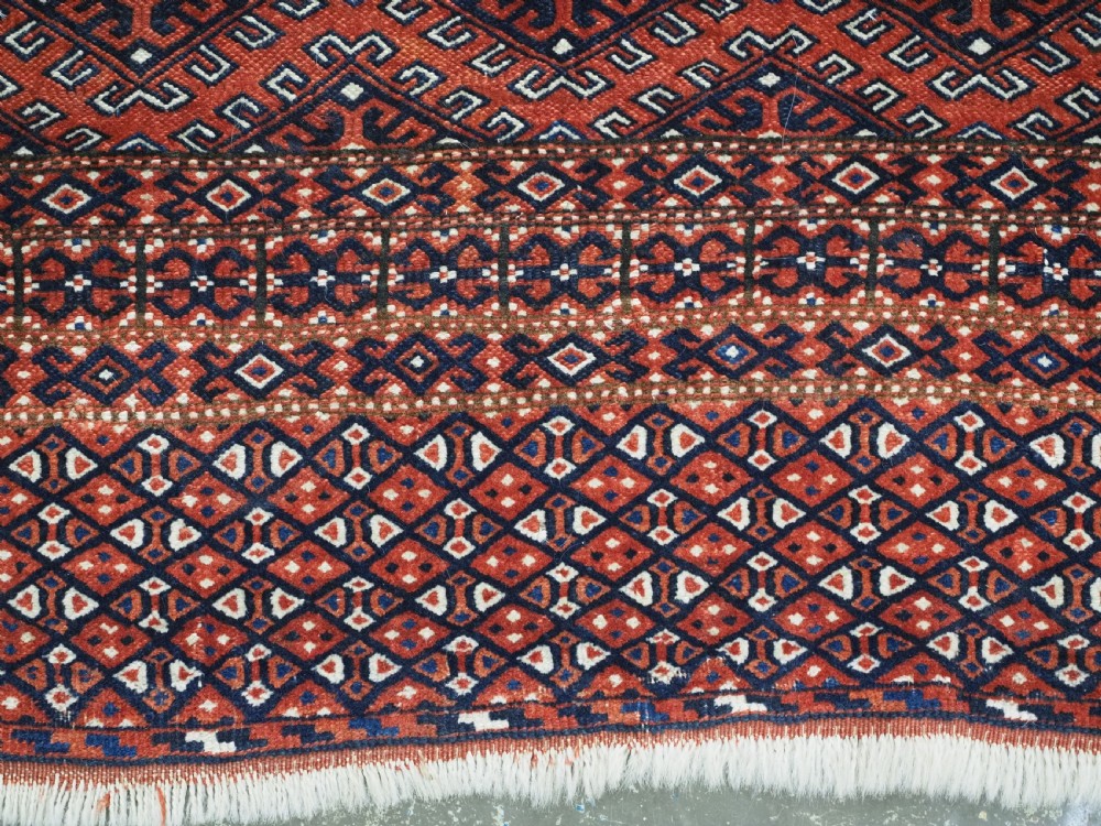 A hand-knotted wool Yomut Turkmen rug featuring a deep red field decorated with a dense repeating lattice pattern in navy, ivory, and brown tones. View X