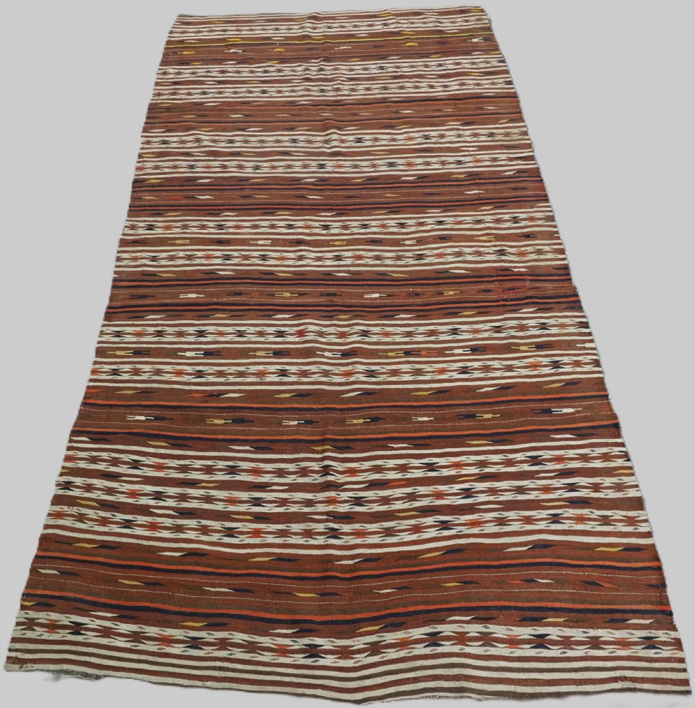 An antique flatweave Turkmen Dali wool kilim rug featuring horizontal bands of terracotta brown, cream, ochre, and dark navy geometric patterns.