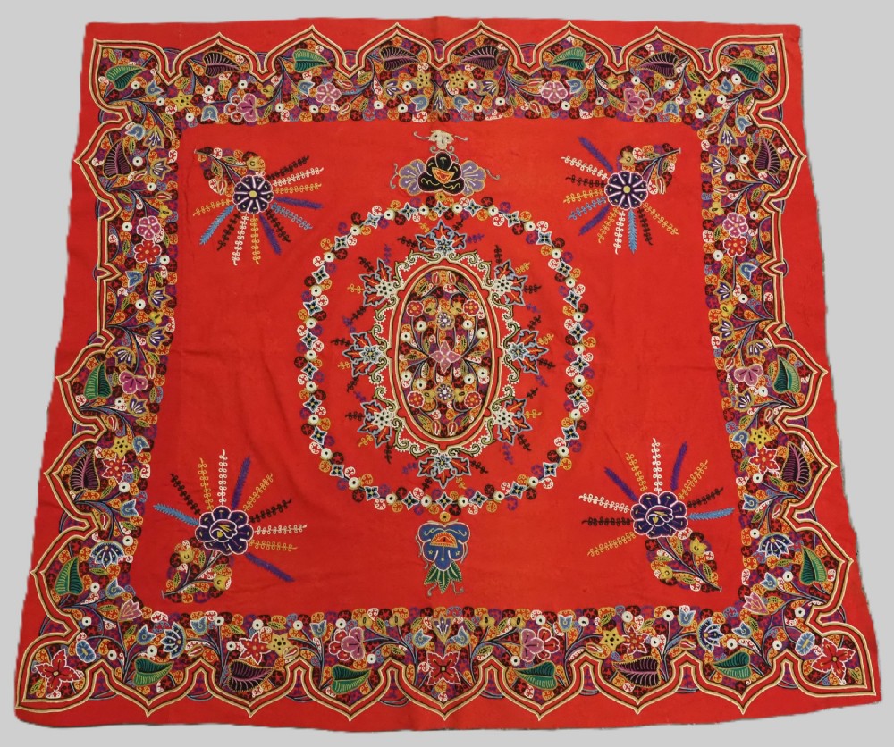 A square red felt textile decorated with polychrome silk chain-stitch embroidery and floral medallion applique motifs.