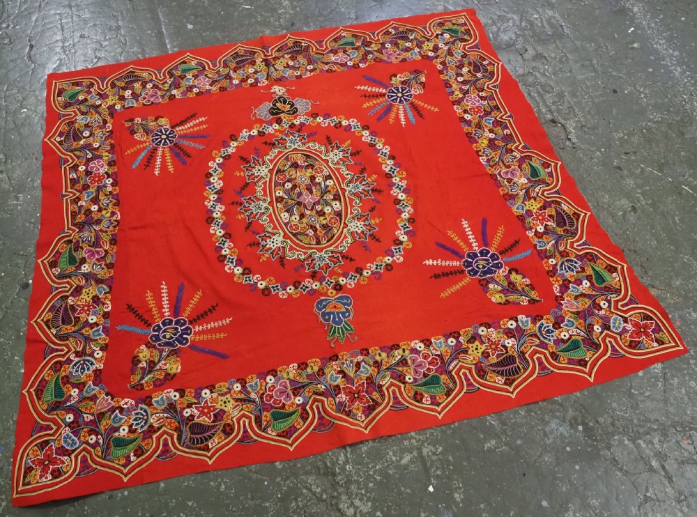 A square red felt textile decorated with polychrome silk chain-stitch embroidery and floral medallion applique motifs. View III