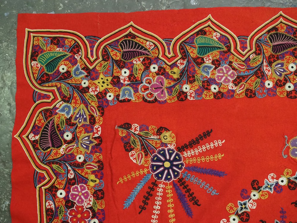 A square red felt textile decorated with polychrome silk chain-stitch embroidery and floral medallion applique motifs. View IV