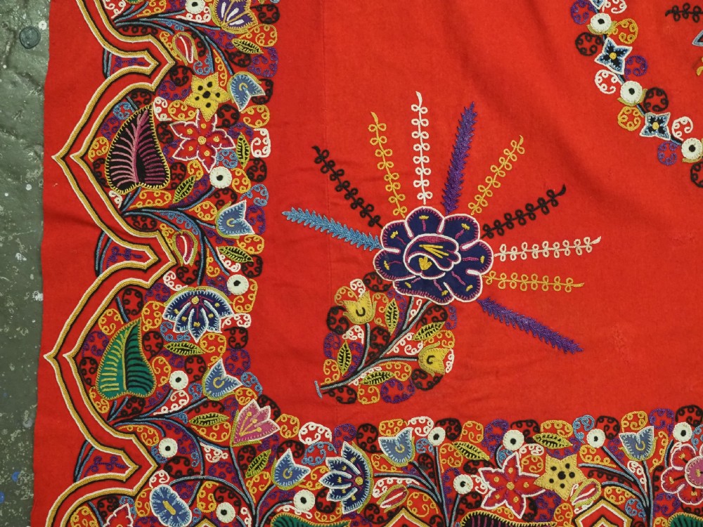 A square red felt textile decorated with polychrome silk chain-stitch embroidery and floral medallion applique motifs. View V