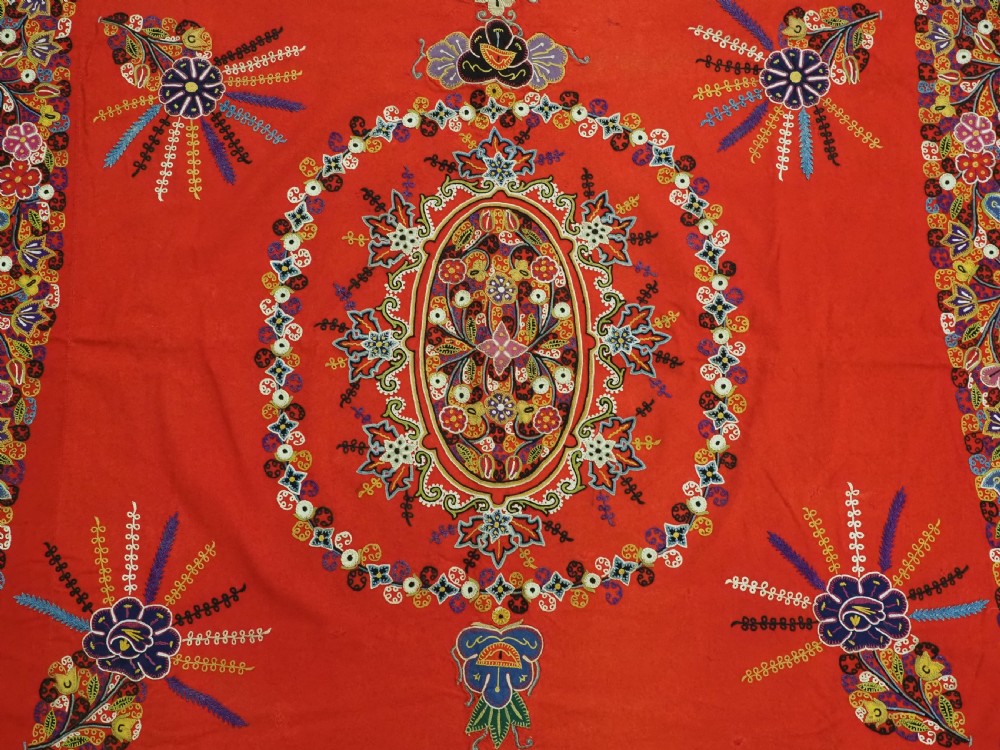 A square red felt textile decorated with polychrome silk chain-stitch embroidery and floral medallion applique motifs. View VI