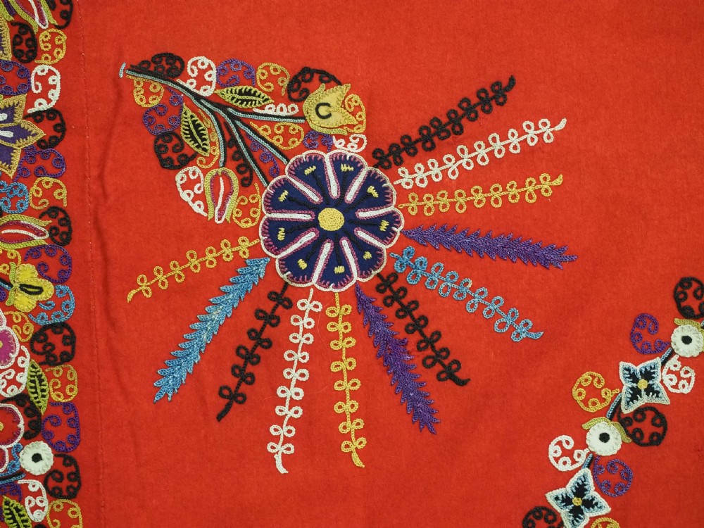 A square red felt textile decorated with polychrome silk chain-stitch embroidery and floral medallion applique motifs. View VII