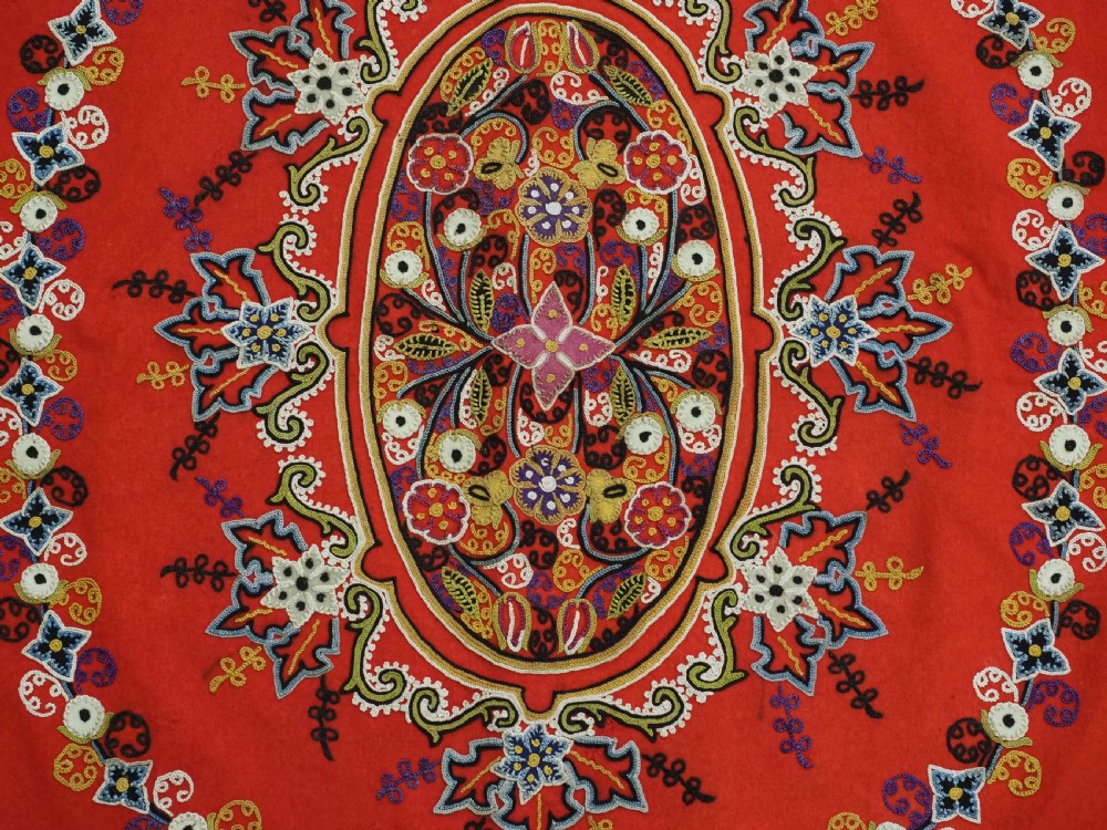 A square red felt textile decorated with polychrome silk chain-stitch embroidery and floral medallion applique motifs. View IX
