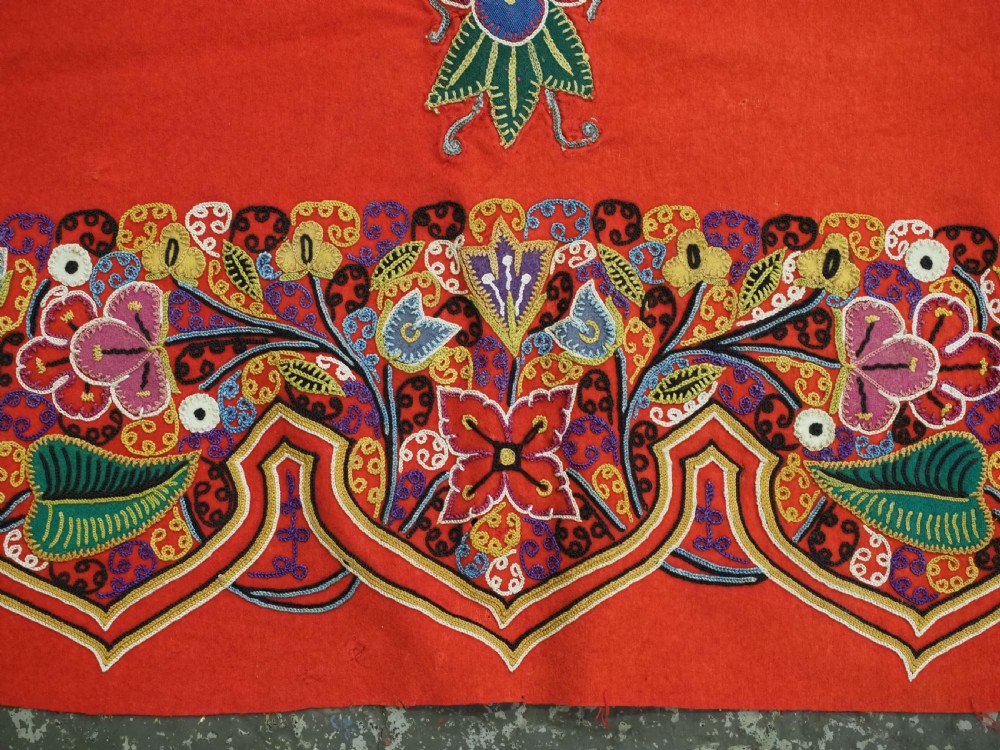 A square red felt textile decorated with polychrome silk chain-stitch embroidery and floral medallion applique motifs. View X