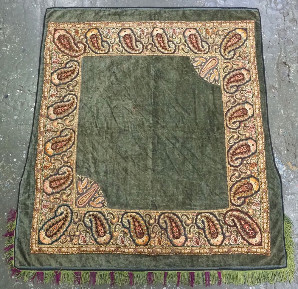 An antique rectangular olive green velvet textile decorated with intricate silk paisley embroidered borders and a fringed edge.