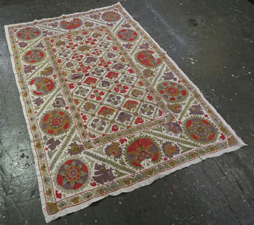 A rectangular embroidered suzani textile featuring a central diamond lattice pattern surrounded by a border of large floral medallions on a cream background. View II