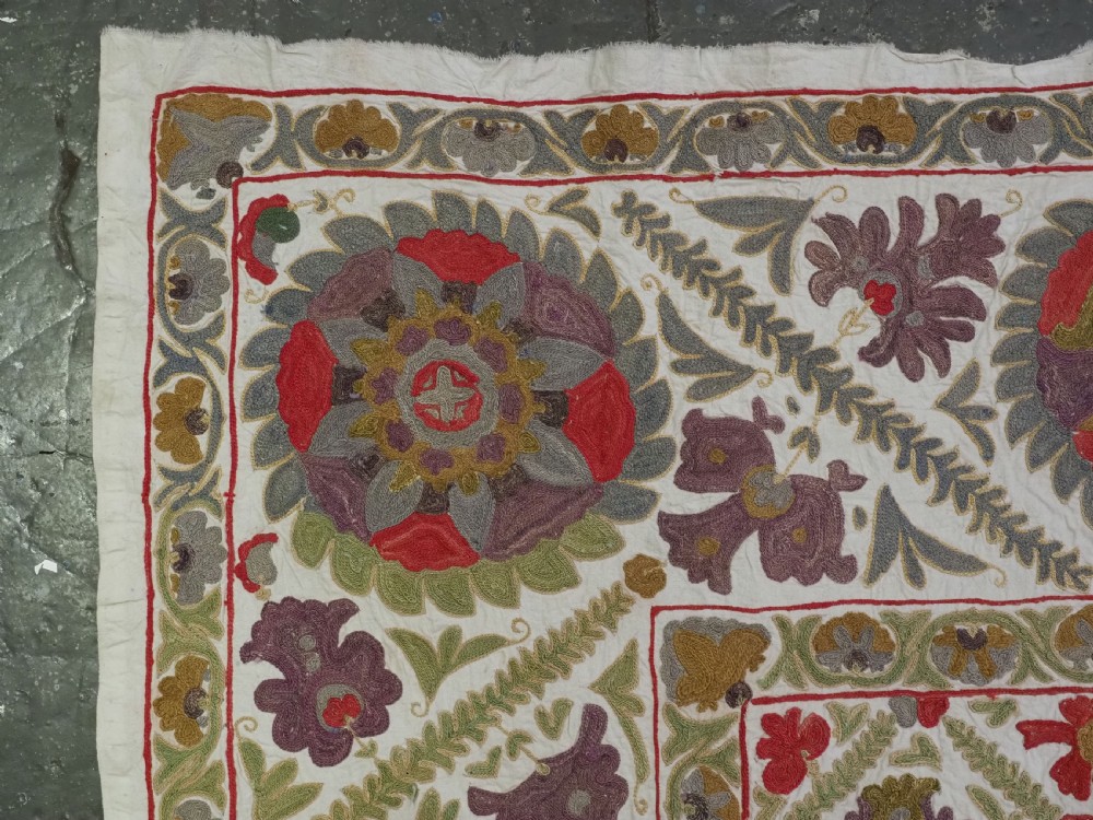 A rectangular embroidered suzani textile featuring a central diamond lattice pattern surrounded by a border of large floral medallions on a cream background. View VI
