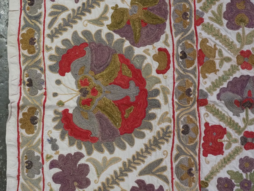 A rectangular embroidered suzani textile featuring a central diamond lattice pattern surrounded by a border of large floral medallions on a cream background. View VII