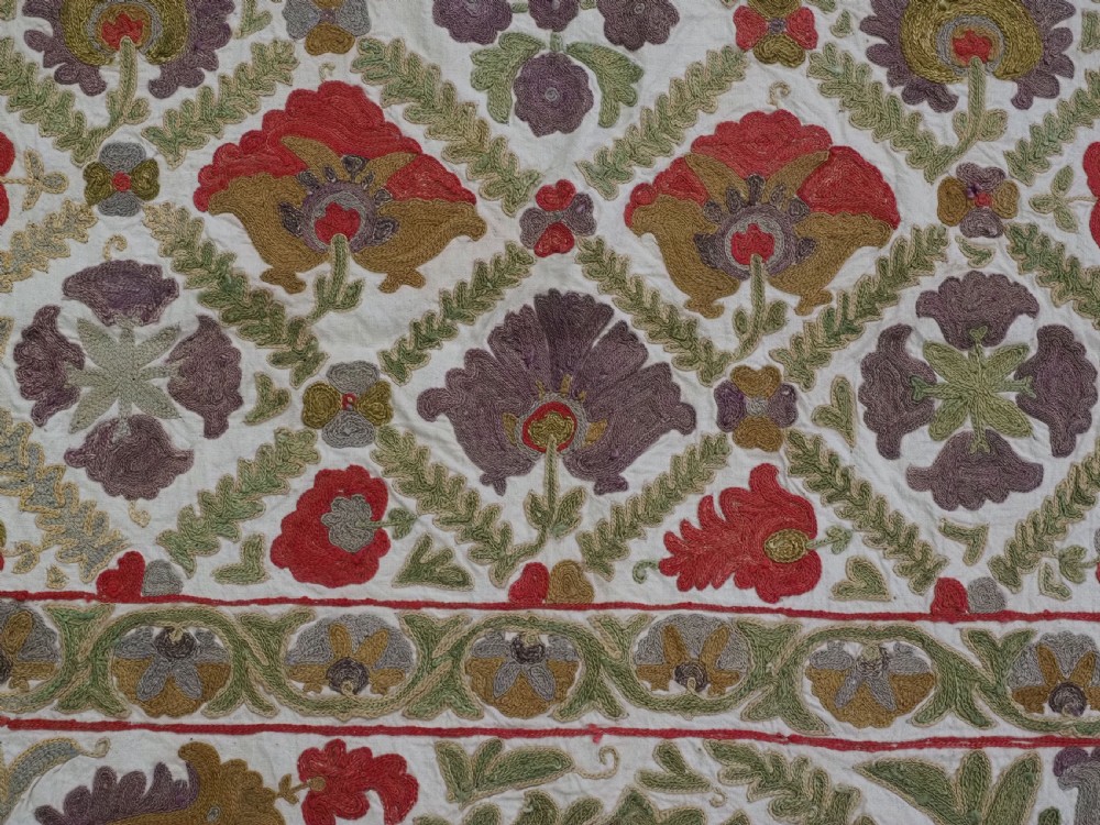 A rectangular embroidered suzani textile featuring a central diamond lattice pattern surrounded by a border of large floral medallions on a cream background. View XI