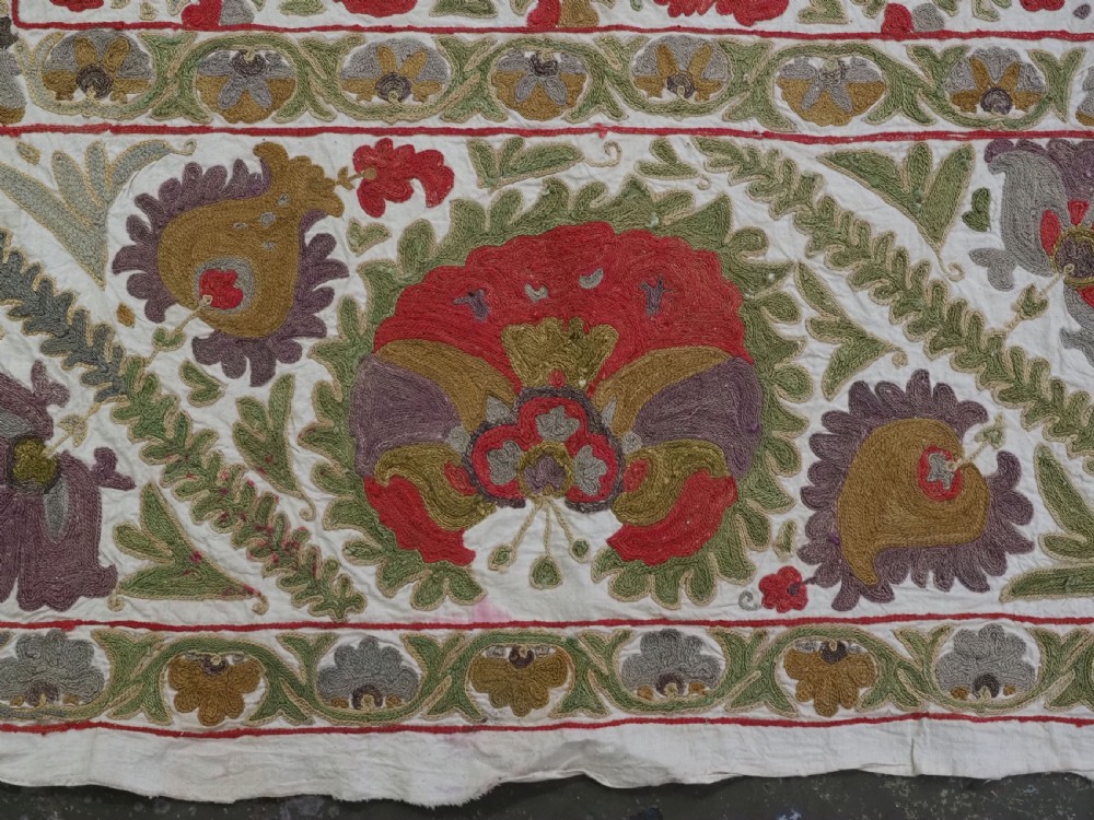 A rectangular embroidered suzani textile featuring a central diamond lattice pattern surrounded by a border of large floral medallions on a cream background. View XII