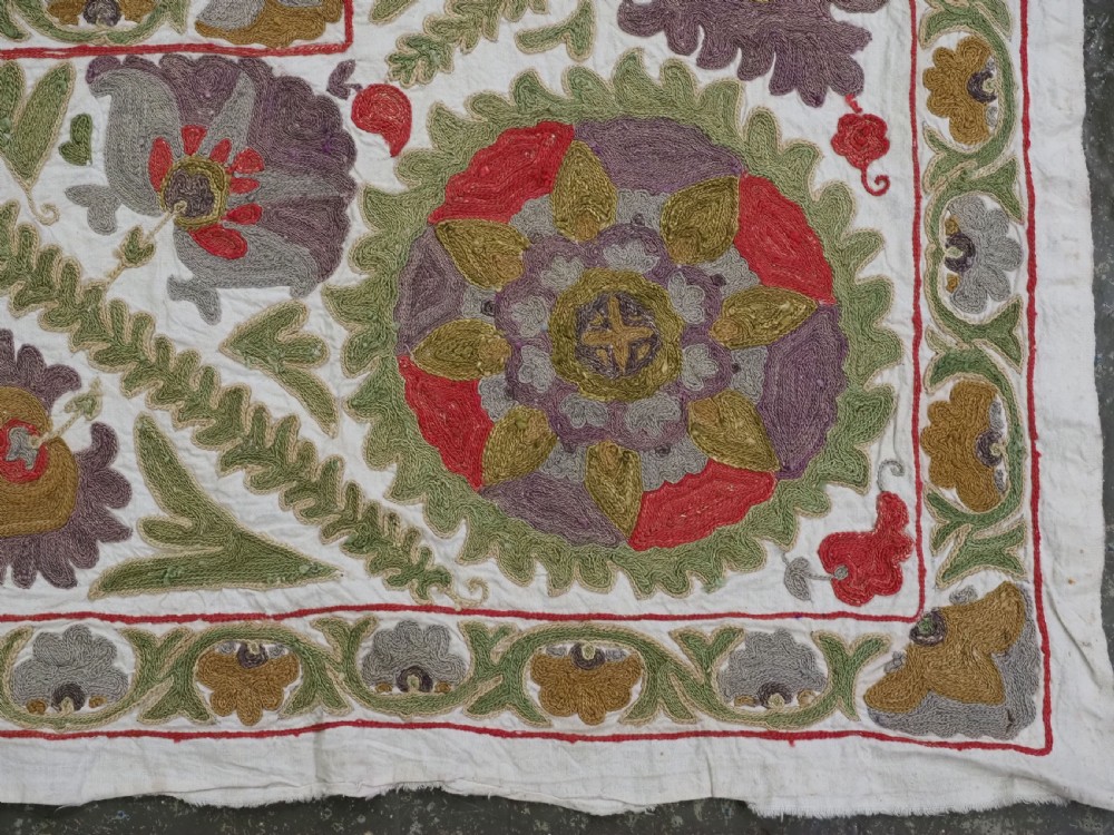 A rectangular embroidered suzani textile featuring a central diamond lattice pattern surrounded by a border of large floral medallions on a cream background. View XIII