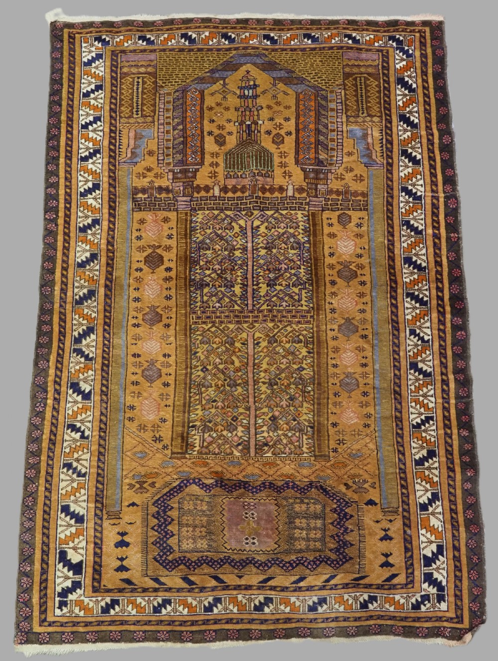 A rectangular handwoven camel wool prayer rug displaying a stylized central mihrab arch motif and geometric decorative borders.