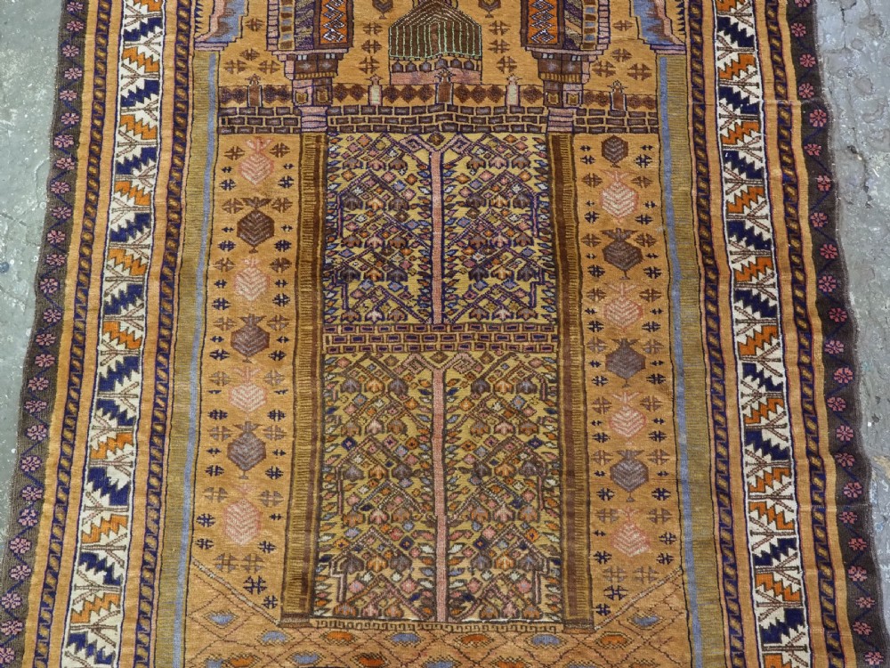 A rectangular handwoven camel wool prayer rug displaying a stylized central mihrab arch motif and geometric decorative borders. View IV