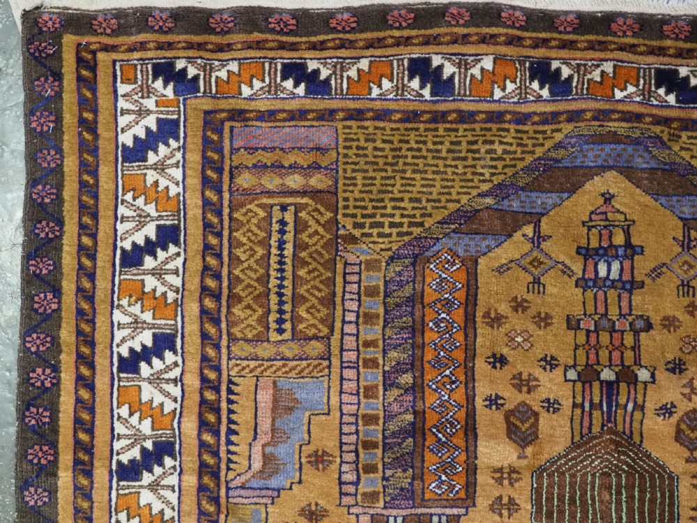 A rectangular handwoven camel wool prayer rug displaying a stylized central mihrab arch motif and geometric decorative borders. View V