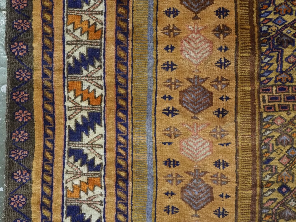 A rectangular handwoven camel wool prayer rug displaying a stylized central mihrab arch motif and geometric decorative borders. View VI