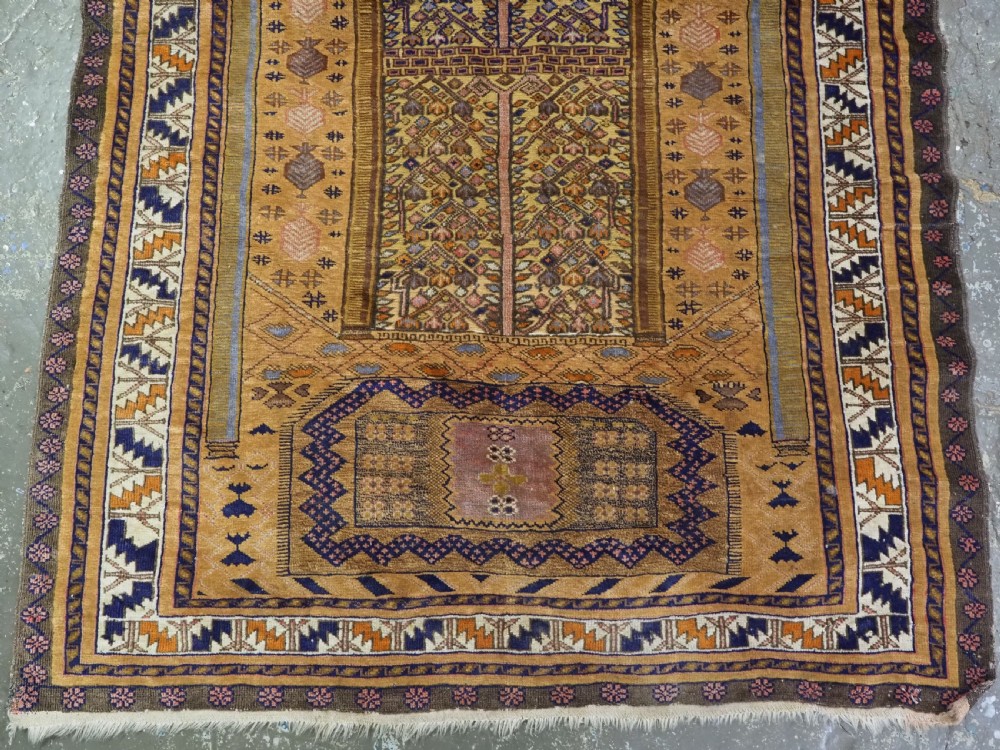 A rectangular handwoven camel wool prayer rug displaying a stylized central mihrab arch motif and geometric decorative borders. View VII
