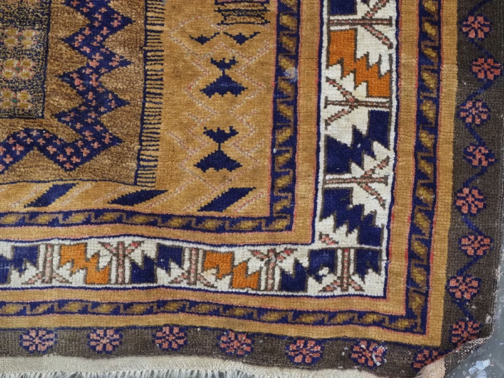 A rectangular handwoven camel wool prayer rug displaying a stylized central mihrab arch motif and geometric decorative borders. View XII