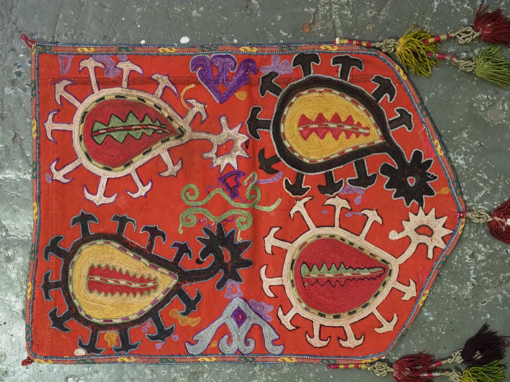 An antique Uzbek shield-shaped red wool textile embroidered with colourful silk teardrop motifs and finished with hanging wool tassels. View II