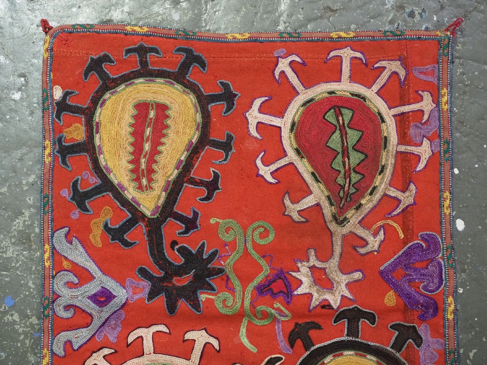 An antique Uzbek shield-shaped red wool textile embroidered with colourful silk teardrop motifs and finished with hanging wool tassels. View III
