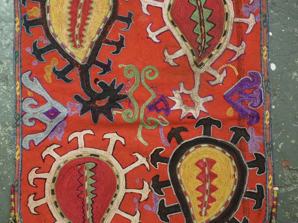 An antique Uzbek shield-shaped red wool textile embroidered with colourful silk teardrop motifs and finished with hanging wool tassels. View IV