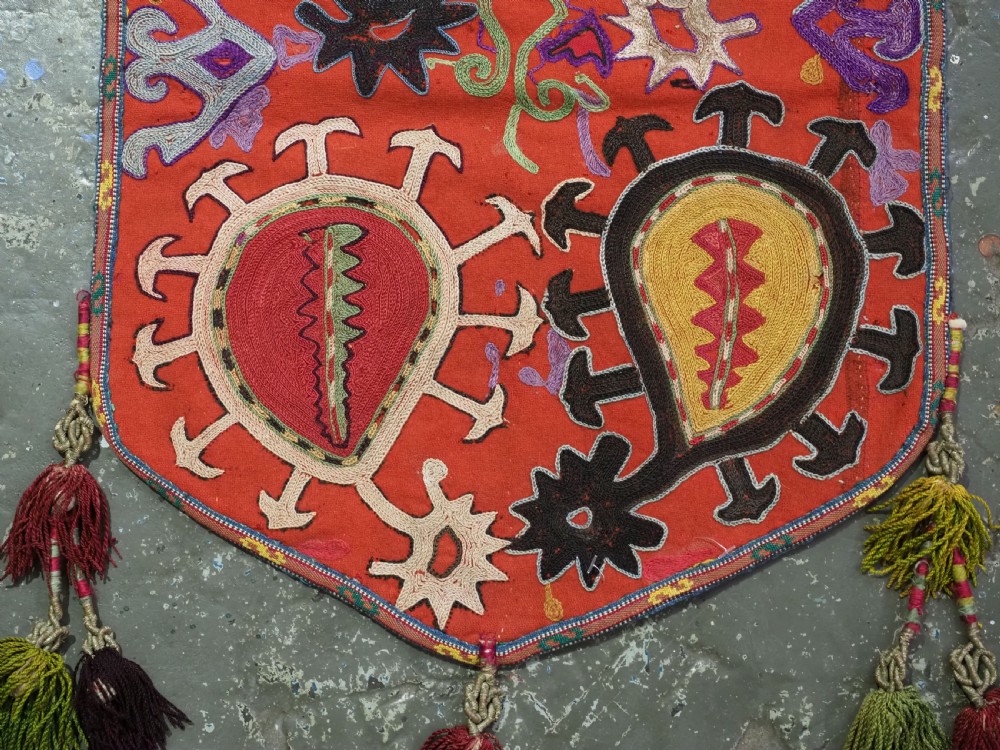 An antique Uzbek shield-shaped red wool textile embroidered with colourful silk teardrop motifs and finished with hanging wool tassels. View V