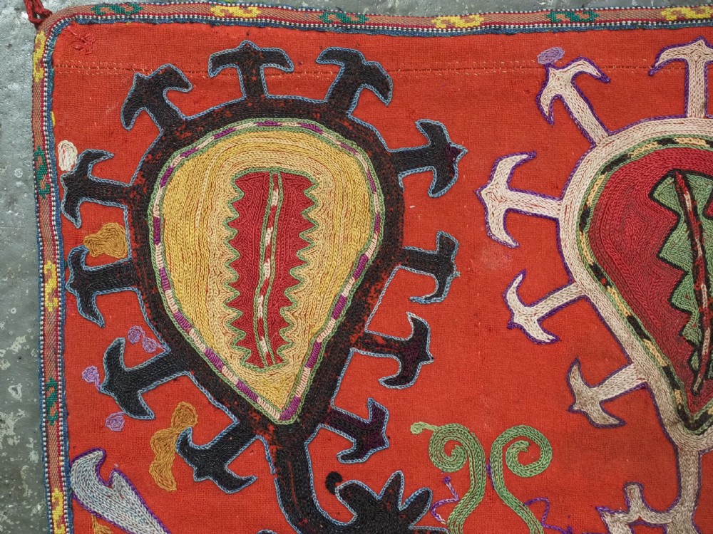 An antique Uzbek shield-shaped red wool textile embroidered with colourful silk teardrop motifs and finished with hanging wool tassels. View VI