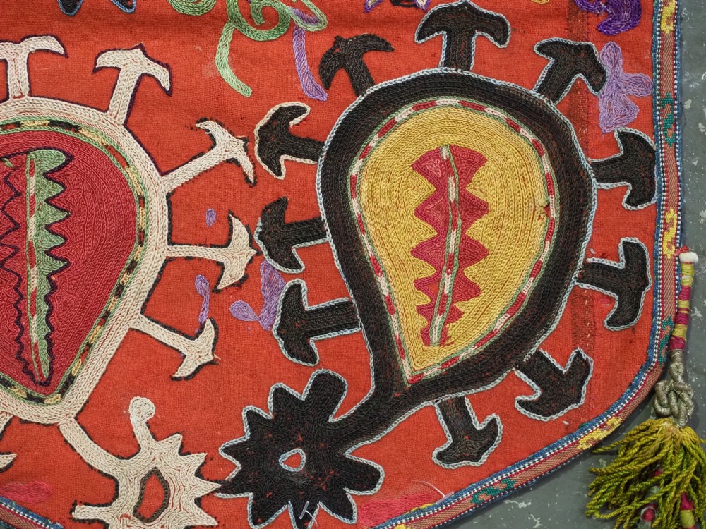 An antique Uzbek shield-shaped red wool textile embroidered with colourful silk teardrop motifs and finished with hanging wool tassels. View VII