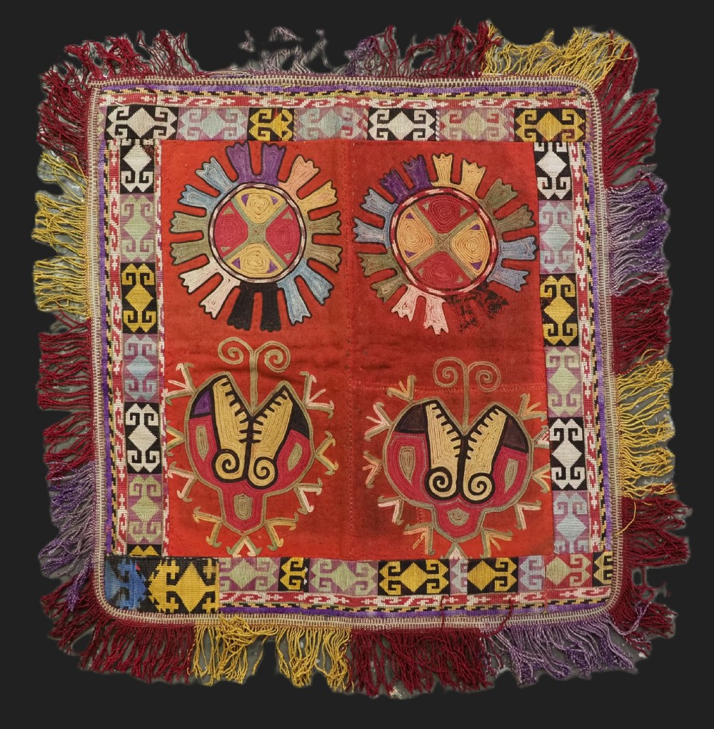 A square red embroidered Uzbek Lakai tribal ilgich wall hanging featuring solar medallions, geometric borders, and coloured fringe.