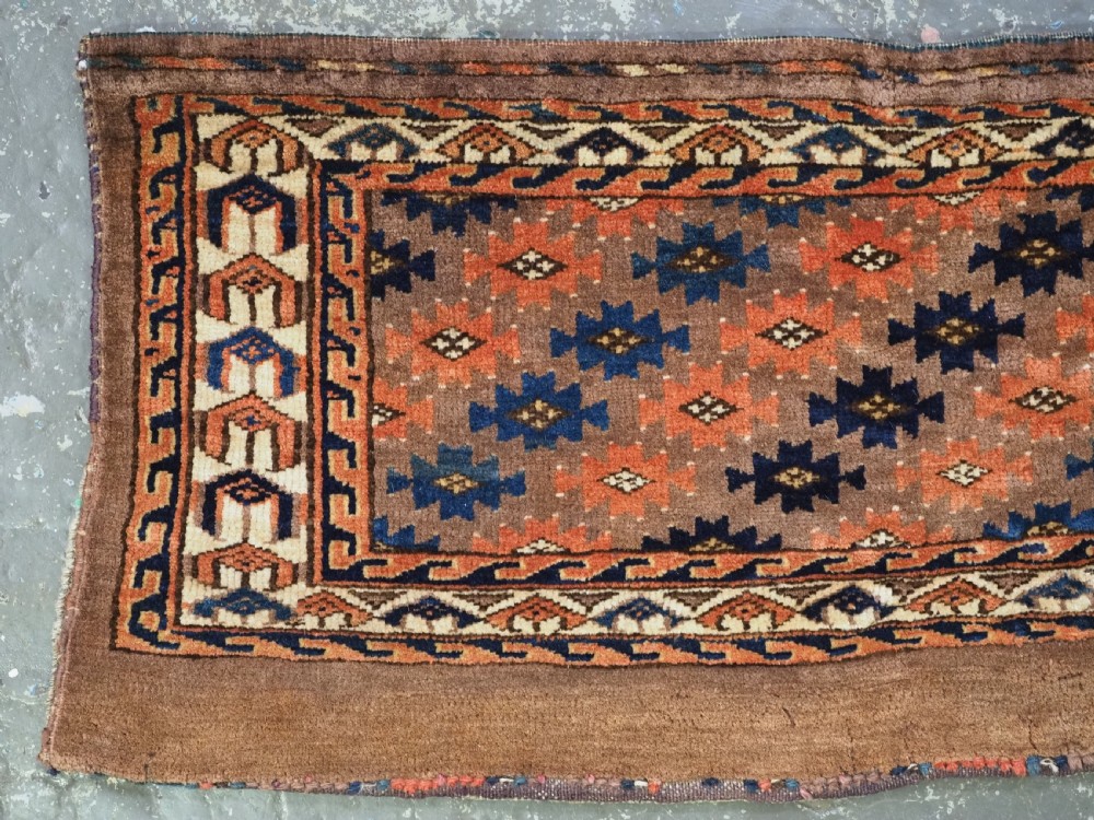 An antique woven Yomut Turkmen torba displaying repeated geometric Aishk gul patterns in red, blue, and ivory on a warm brown background. View II