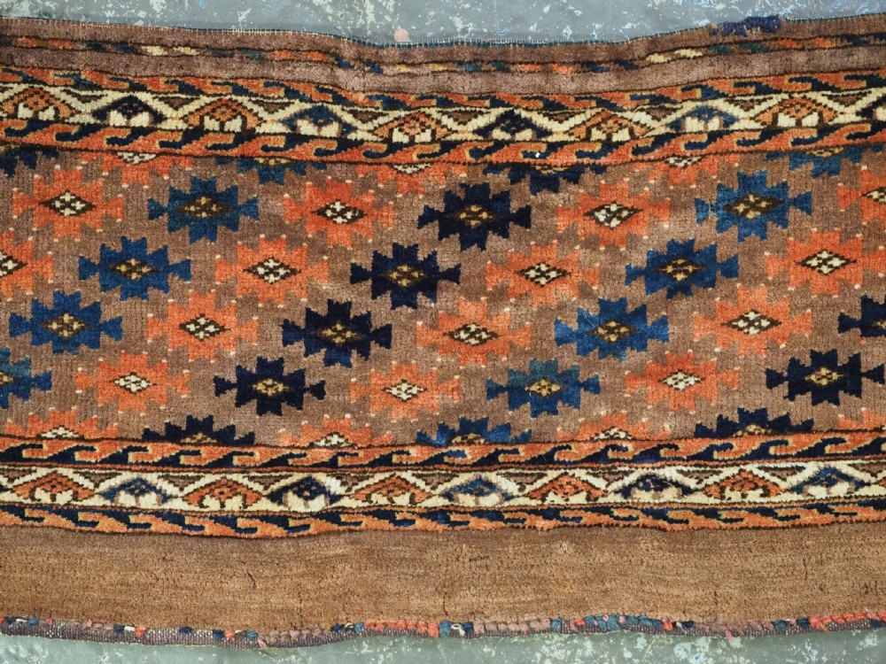 An antique woven Yomut Turkmen torba displaying repeated geometric Aishk gul patterns in red, blue, and ivory on a warm brown background. View III
