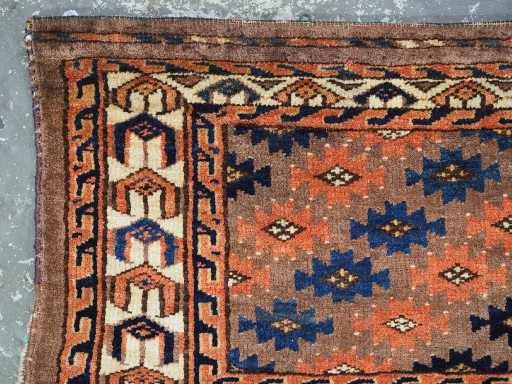 An antique woven Yomut Turkmen torba displaying repeated geometric Aishk gul patterns in red, blue, and ivory on a warm brown background. View V