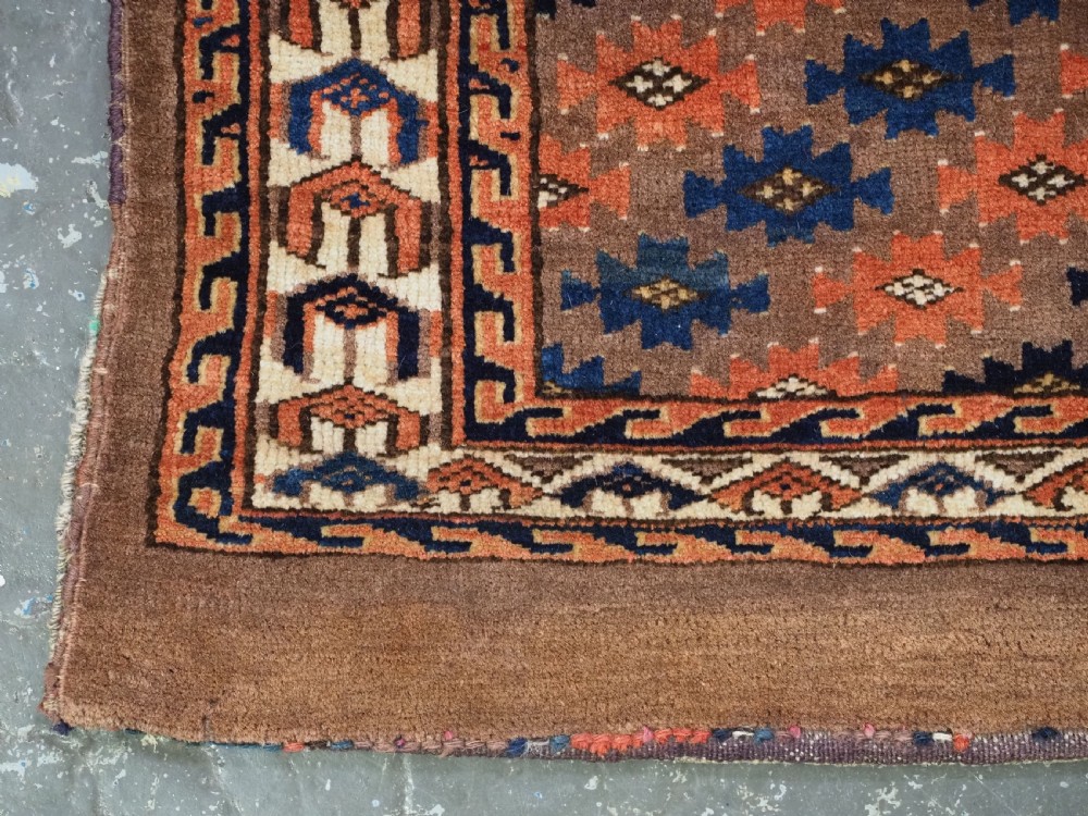 An antique woven Yomut Turkmen torba displaying repeated geometric Aishk gul patterns in red, blue, and ivory on a warm brown background. View VI