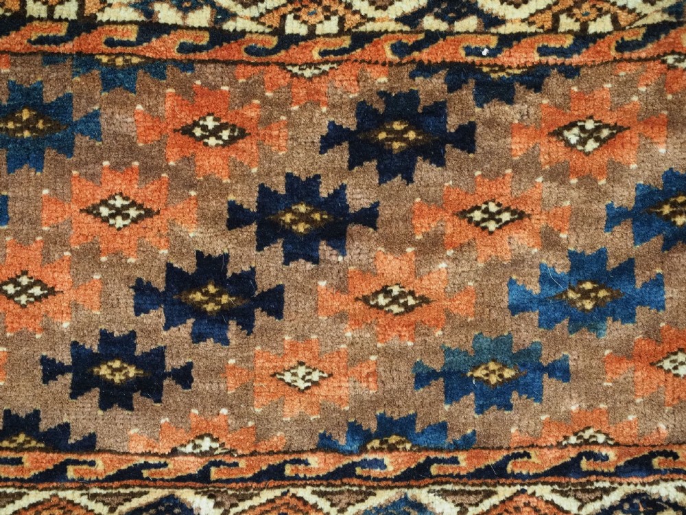 An antique woven Yomut Turkmen torba displaying repeated geometric Aishk gul patterns in red, blue, and ivory on a warm brown background. View VII