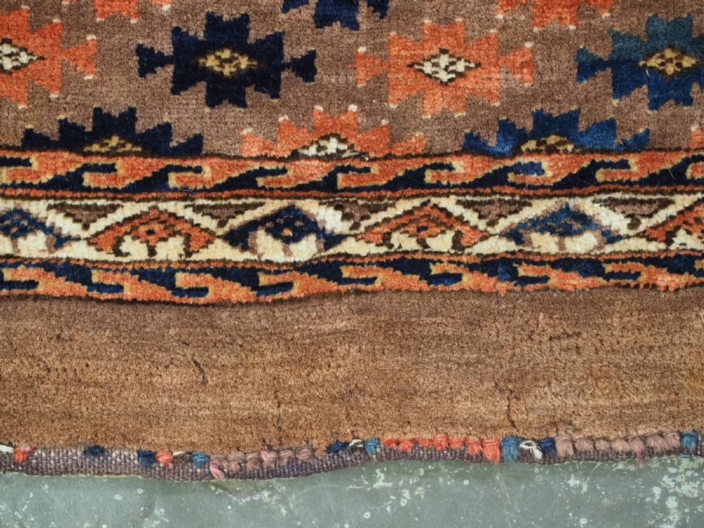 An antique woven Yomut Turkmen torba displaying repeated geometric Aishk gul patterns in red, blue, and ivory on a warm brown background. View VIII