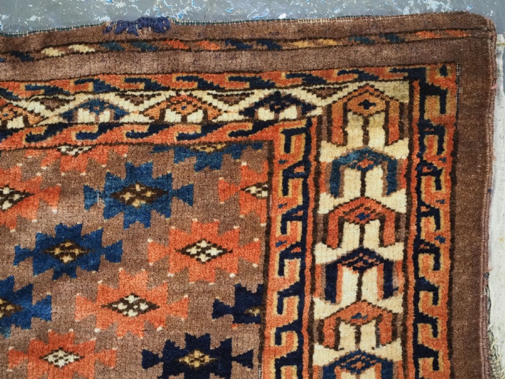 An antique woven Yomut Turkmen torba displaying repeated geometric Aishk gul patterns in red, blue, and ivory on a warm brown background. View IX
