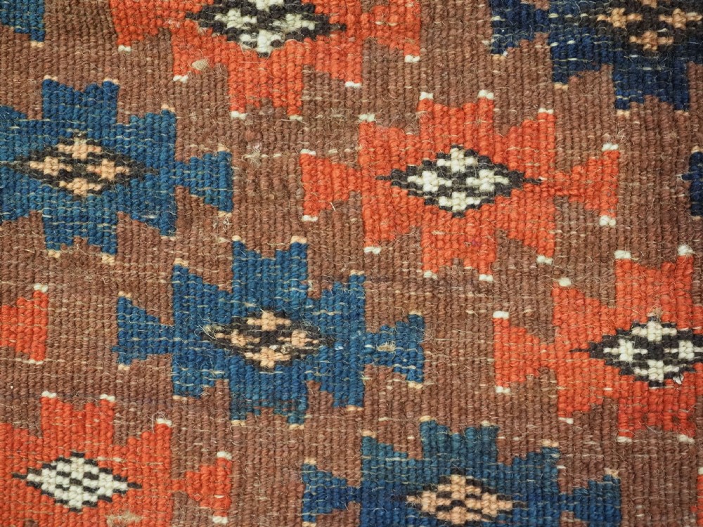 An antique woven Yomut Turkmen torba displaying repeated geometric Aishk gul patterns in red, blue, and ivory on a warm brown background. View X