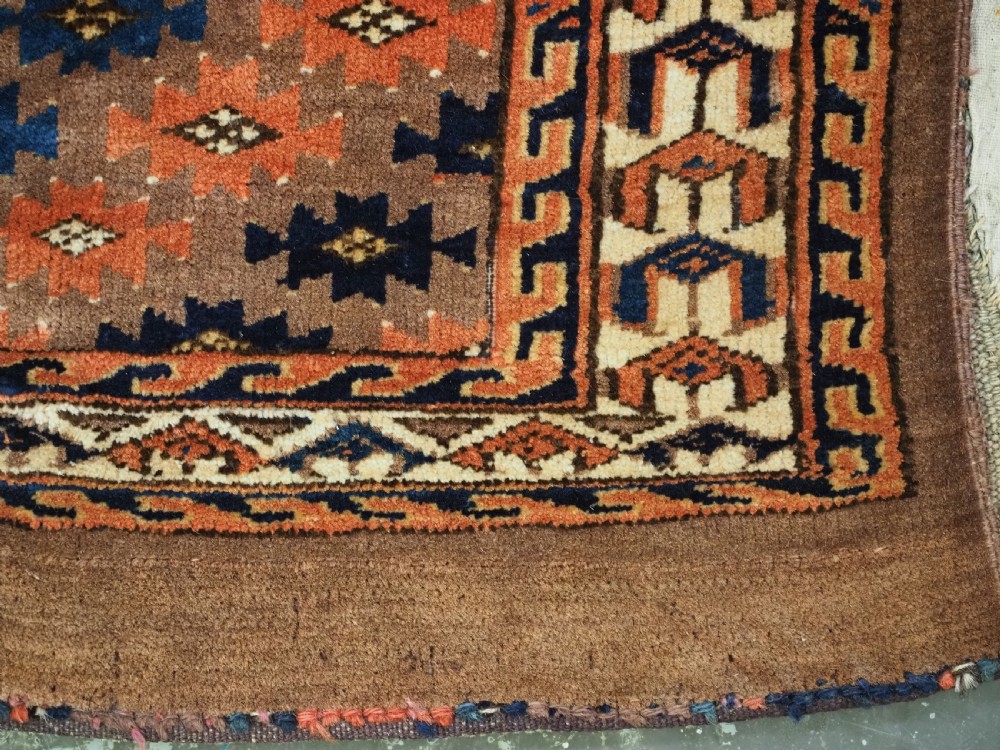 An antique woven Yomut Turkmen torba displaying repeated geometric Aishk gul patterns in red, blue, and ivory on a warm brown background. View XIII