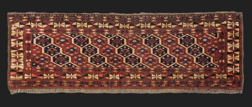 A horizontal woven antique Turkmen torba panel in deep terracotta red, navy blue, and cream, featuring repeating geometric octagonal Schemle gul motifs across the field.