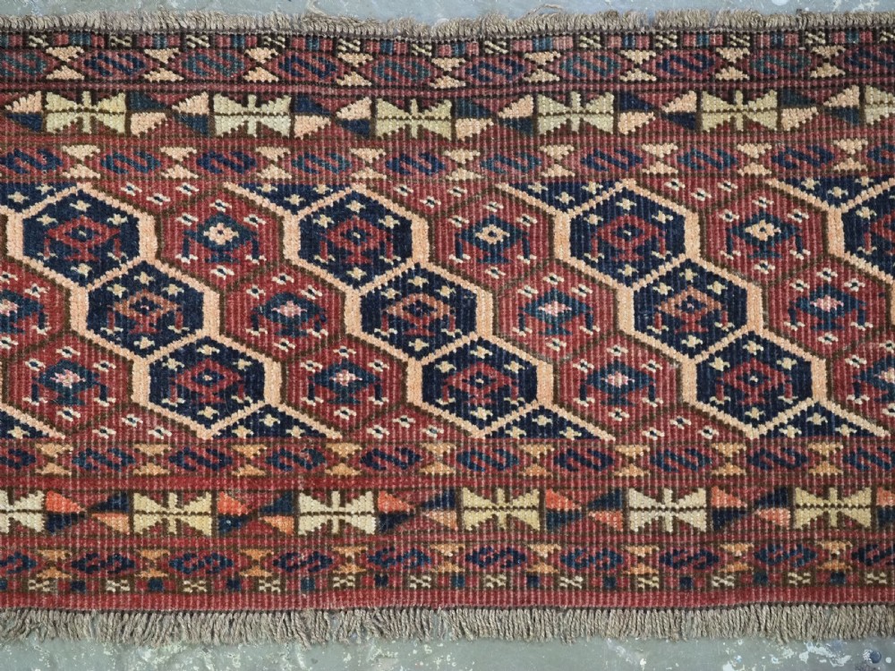 A horizontal woven antique Turkmen torba panel in deep terracotta red, navy blue, and cream, featuring repeating geometric octagonal Schemle gul motifs across the field. View III